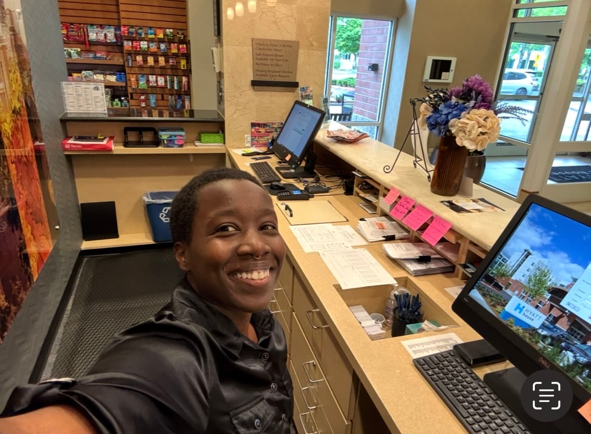 Holly smiling at the Hyatt House front desk, with the reception counter and lobby behind her