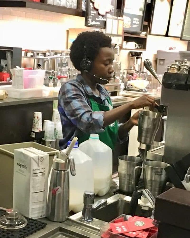 Holly steaming milk behind the espresso bar as a Starbucks barista, wearing a green apron and headset