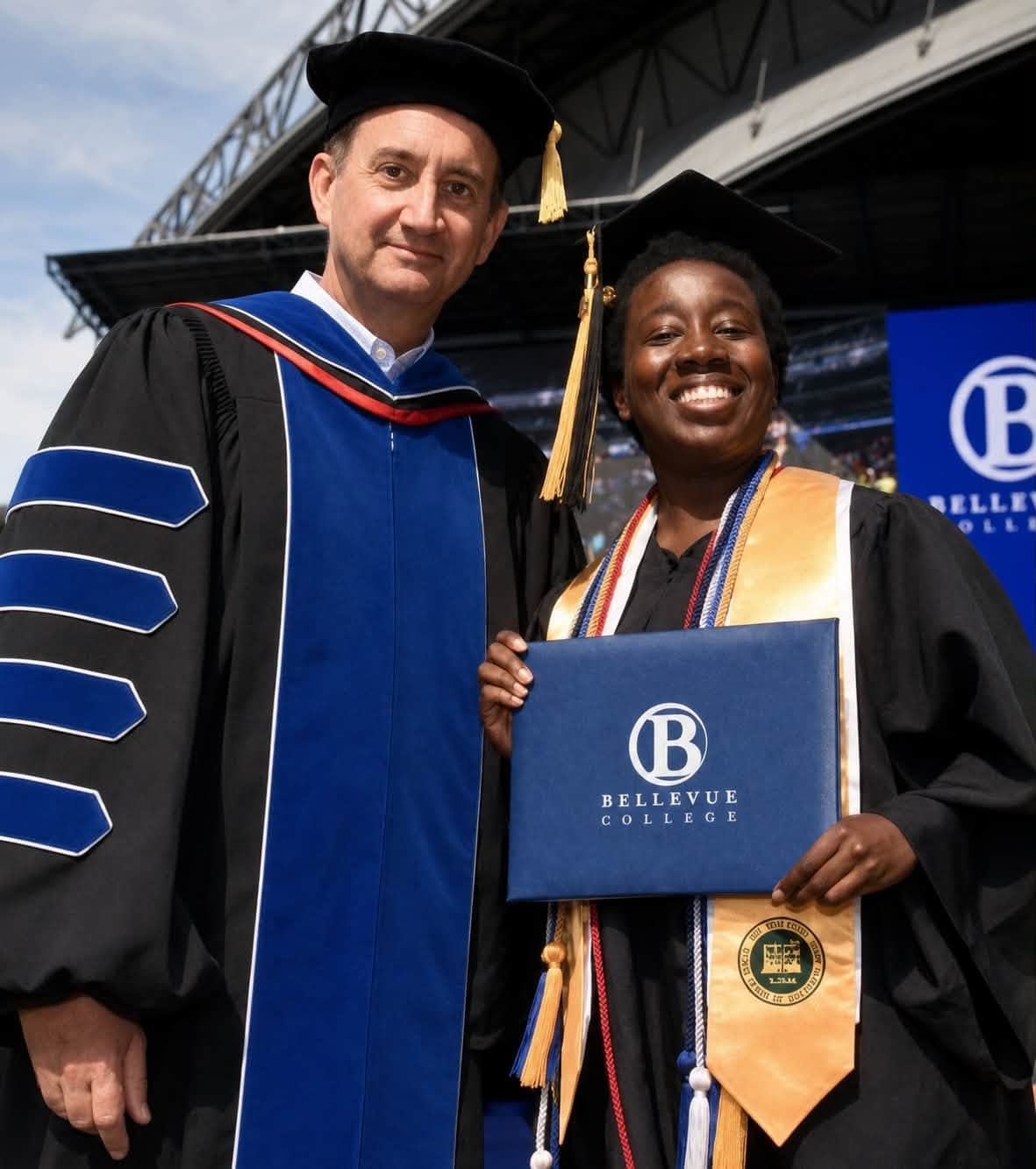 Holly in a cap and gown holding her Bellevue College diploma on stage at graduation